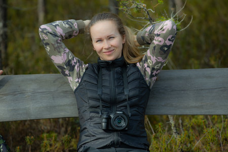 Young woman sitting on a fence in the woods with a camera.の写真素材