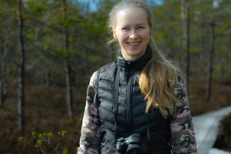 Beautiful young woman with a camera in the spring forest. Selective focus.の写真素材