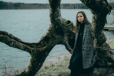 Young beautiful girl in a long black dress and a plaid shirt on the background of the lakeの写真素材