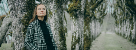 Beautiful girl in a plaid coat walks through the forest.の写真素材