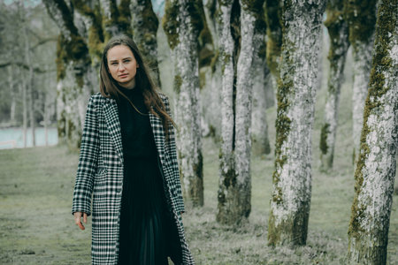 Portrait of a beautiful girl in a long black dress and a checkered coat in the forest.の写真素材