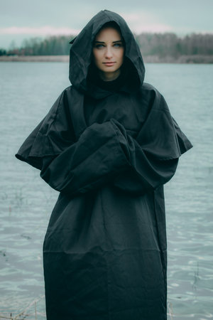 Portrait of a young woman in a black raincoat on the lakeの写真素材