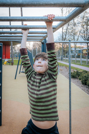 A boy is doing pull-ups on the sports ground in the parkの写真素材
