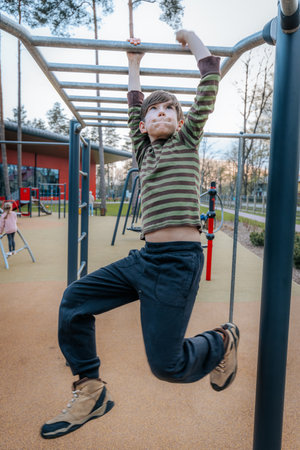 cute little boy doing pull ups on sports ground in autumn park