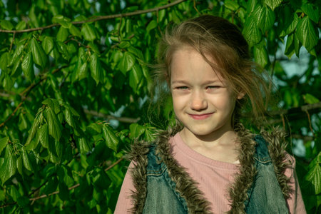 Portrait of a little girl on a background of green leaves.の写真素材