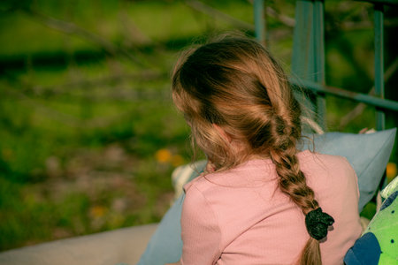 A little girl is sitting on a swing in the garden. Selective focus.の写真素材