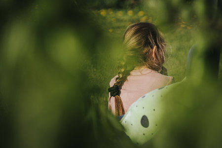 Little girl sitting in a chair in the garden and looking through the windowの写真素材