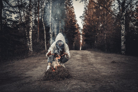A man in a hood with a bonfire in the forest.の写真素材