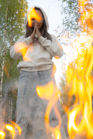 Young woman in a white sweater and jeans with a hood on her head is burning in the forest.の写真素材