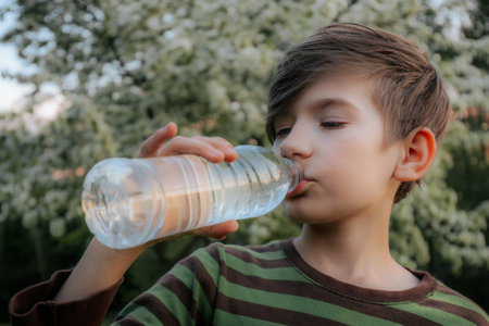 boy drinks water from a plastic bottle in the park in the summerの写真素材