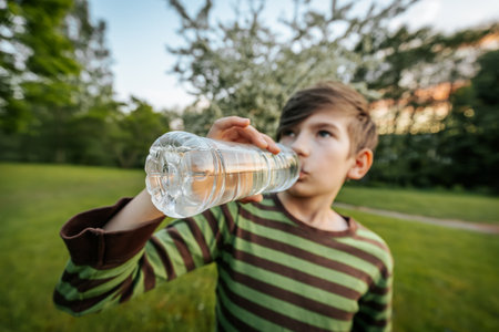 A boy drinks water from a plastic bottle in the park. Selective focus.の写真素材