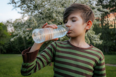 boy drinks water from a plastic bottle in the park on a sunny dayの写真素材