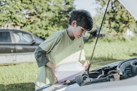 young boy looking under hood of broken car and looking at engine oilの写真素材
