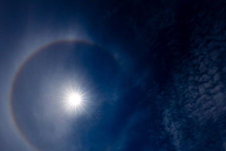 Sun halo over the blue sky with white clouds and sun raysの写真素材