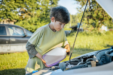 little boy looking at engine oil in car hood while standing on grassの写真素材