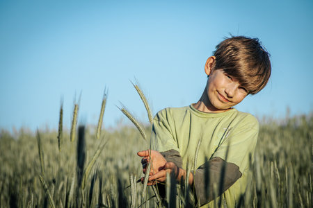 Young boy in green shirt standing in wheat field and looking at cameraの写真素材