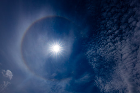 Sun halo in the blue sky with white clouds and sun raysの写真素材