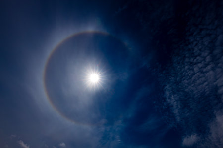 Sun halo in the blue sky with white clouds and sun raysの写真素材