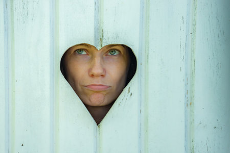 Portrait of a young woman looking through a hole in a wooden fenceの写真素材