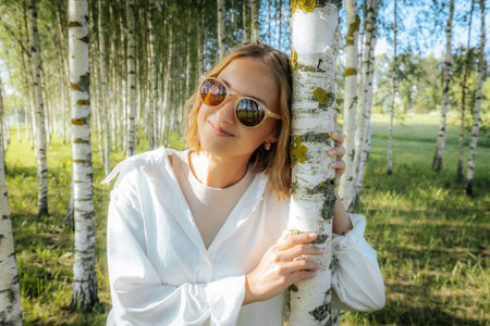 Portrait of a beautiful young woman in sunglasses in a birch groveの写真素材