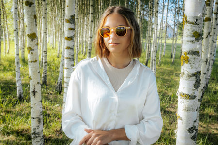 Portrait of a beautiful young woman in a white shirt and sunglasses in a birch groveの写真素材