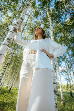 Beautiful girl in a white jumpsuit in the birch forestの写真素材