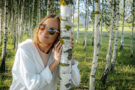 Beautiful girl in a white dress and sunglasses in the birch groveの写真素材