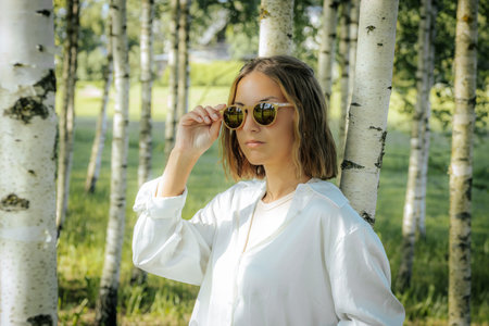 beautiful young woman in a white shirt and sunglasses in the forestの写真素材