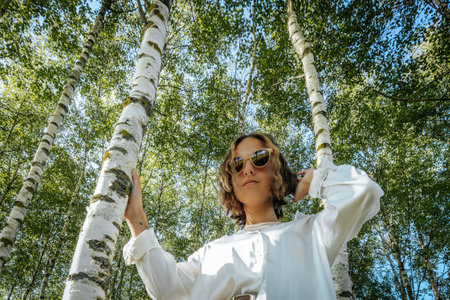 Beautiful girl in a white blouse and sunglasses in a birch groveの写真素材