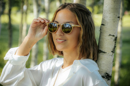 Portrait of a beautiful young woman in sunglasses on a background of trees.の写真素材