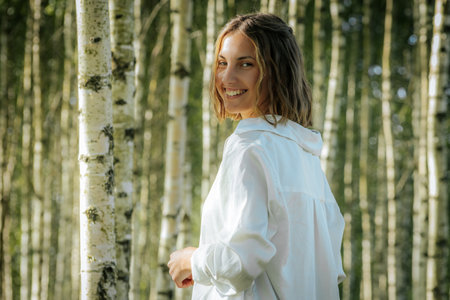 Portrait of a young woman in a white shirt in a birch groveの写真素材