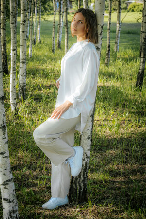 Young beautiful girl in white clothes posing in a birch groveの写真素材