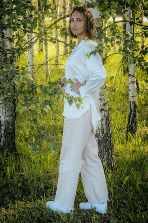 Beautiful young woman in a white suit in a birch groveの写真素材