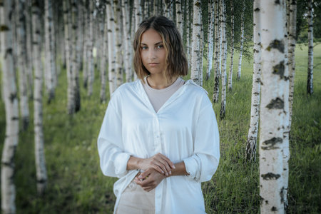 Beautiful young woman in white dress standing in birch forest.の写真素材