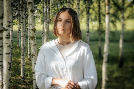 Beautiful young woman in a white shirt in a birch groveの写真素材