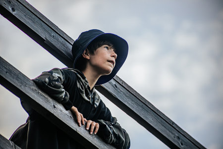 A boy in a black coat and a hat stands on a wooden ladderの写真素材