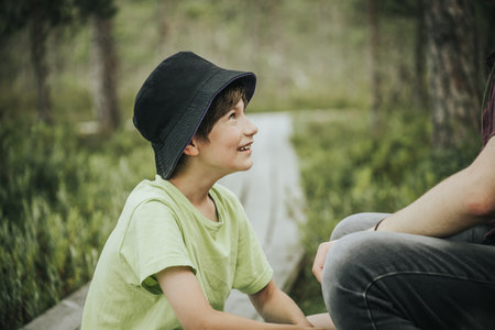 Young boy sitting on a bench in the park with his father.の写真素材