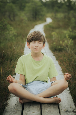 Young boy meditating on a wooden bridge in the summer forest.の写真素材
