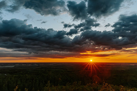 sunset over the forest in summer with dark clouds and rays of lightの写真素材