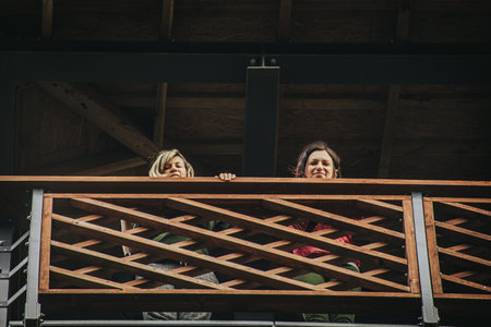 Two women in the balcony of a wooden house in the city.