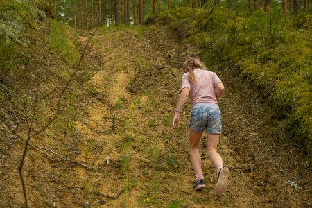 A young woman is walking along a path in the forest. The girl is dressed in shorts and a T-shirt.の写真素材