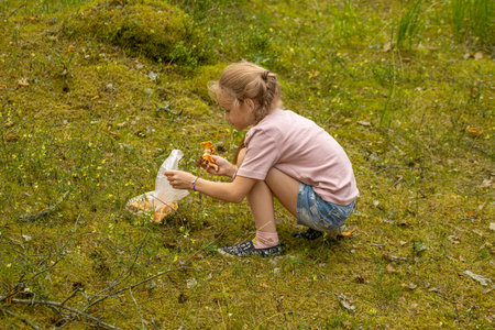 Little girl sitting on the ground and eating mushrooms in the forest.の写真素材