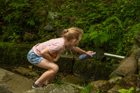 Little girl drinking water from a small fountain in a summer forest.の写真素材