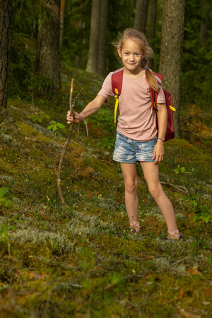 Little girl hiking in the forest with a backpack and a stick.の写真素材
