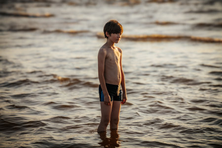 A boy in shorts and a T-shirt swims in the sea at sunsetの写真素材