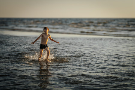 Little boy running and jumping in water on the beach at sunset.の写真素材