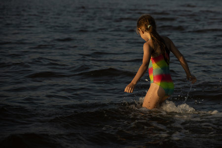 Girl splashing in the sea on a hot summer day, back viewの写真素材