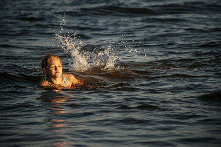 Little girl splashing in the water at sunset. Selective focus.