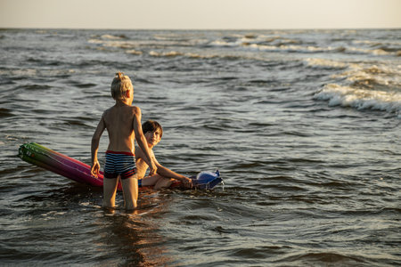 Father and son playing with inflatable ring in sea water at sunsetの写真素材