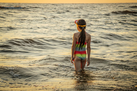 Young girl in a swimsuit on the beach at sunset. Back view.の写真素材